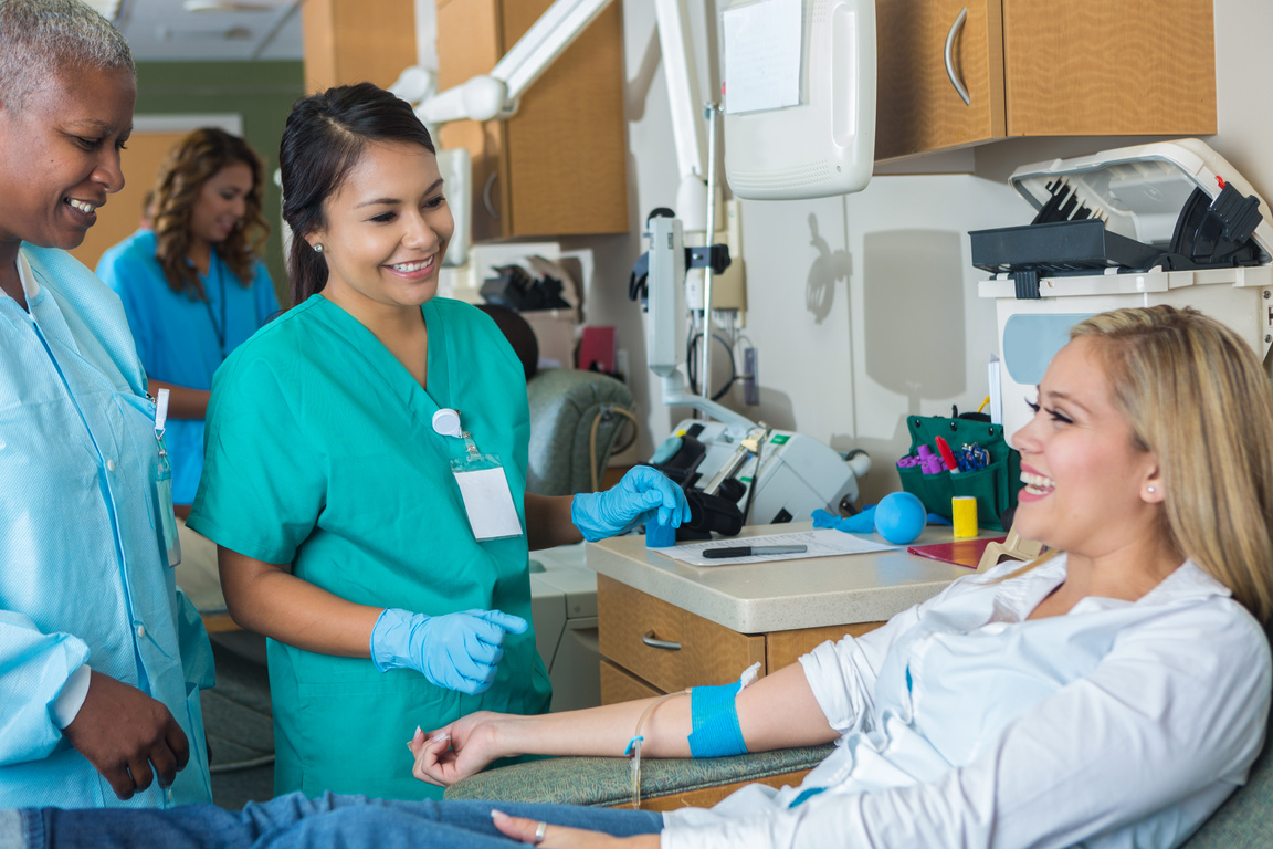 Cheerful female blood donor talks with phlebotomist while donating blood